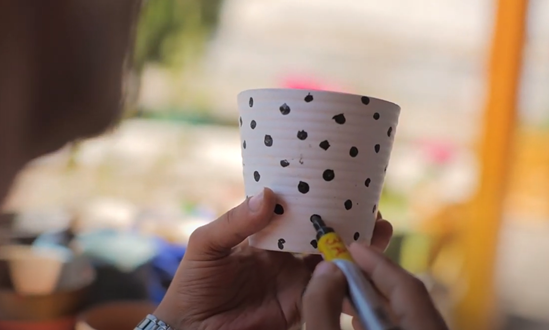 Hand holding and painting dots on a ceramic cup.
